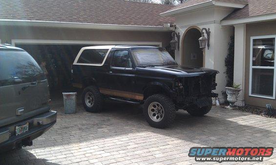 Black 1995 Ford Bronco with white top, missing grille and headlights, parked in driveway