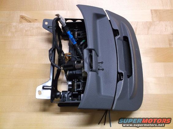 Gray plastic car interior component with exposed wiring and metal bracket, on a wooden surface