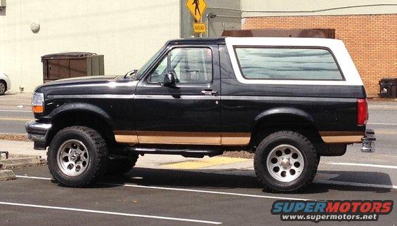 Side view of a black 1995 Ford Bronco with tan trim and a white top