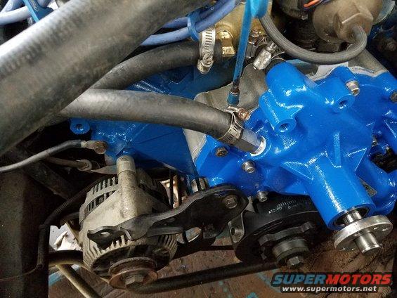 Close-up of engine parts, including an alternator and a blue-painted component, with hoses and wiring visible