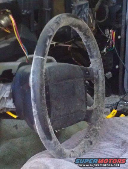 Close-up of a dirty steering wheel with visible wiring and dashboard parts in the background