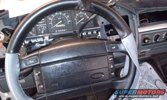 Black steering wheel with gray accents and dashboard gauges in a 1995 Ford Bronco