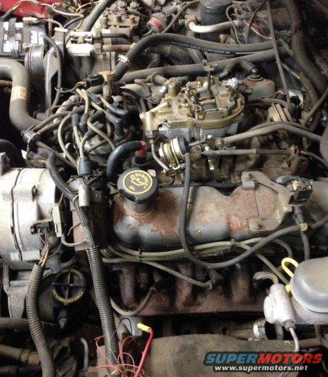 Engine bay with carburetor, alternator, and various hoses and wires