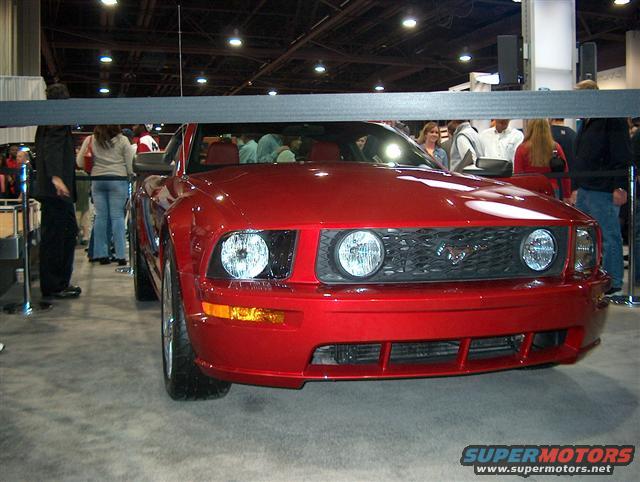 Red Ford Mustang front view, grille with horse emblem, round headlights, at an auto show