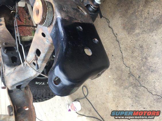 Close-up of vehicle frame and suspension parts, some painted black, on concrete