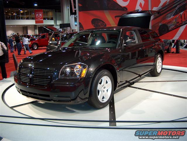 Black Dodge Magnum wagon on a rotating display at an auto show, with other vehicles and Dodge branding in the background