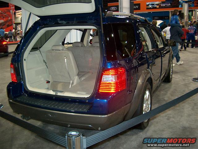 Blue SUV's open tailgate reveals beige interior and folded seats. Rear bumper is dark gray