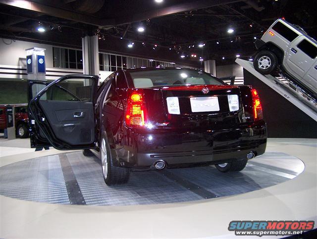 Rear view of black sedan with doors open on a turntable, Hummer on display behind
