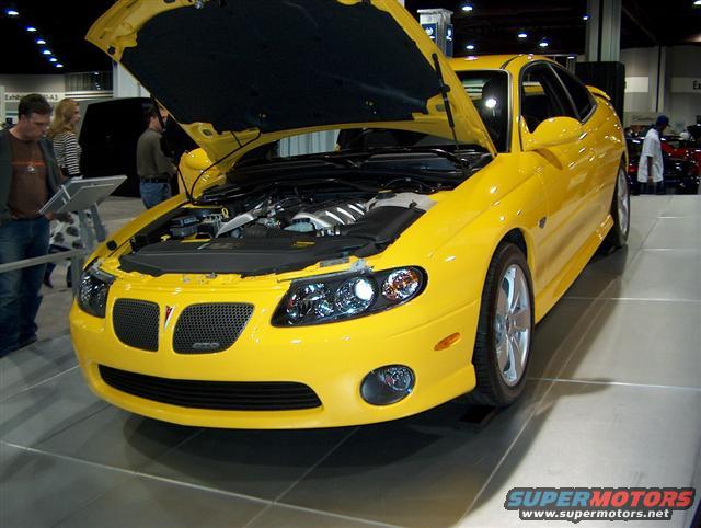 Yellow Pontiac GTO coupe with hood open, showing engine bay. Front grille has GTO badge