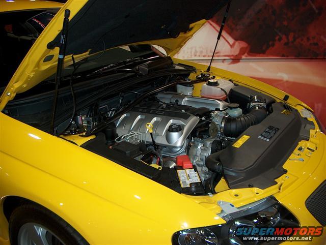 Yellow car's engine bay with hood open. Shows engine, air intake, and battery