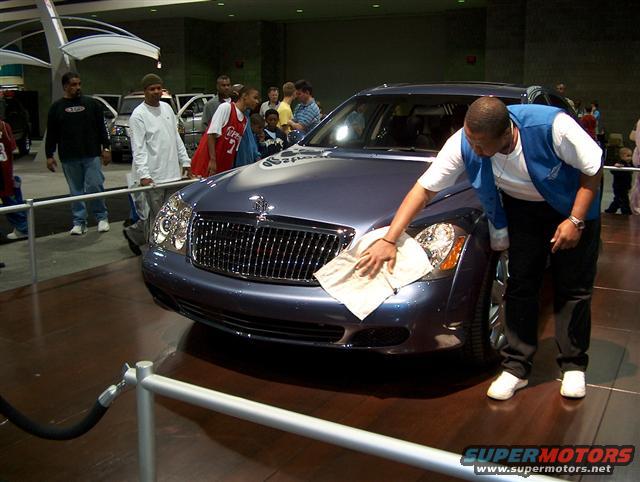 Man cleaning the front of a dark blue luxury sedan with a white cloth at an auto show
