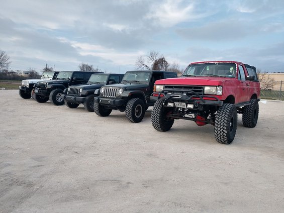 Red SUV with winch and lift kit parked in front of several Jeeps