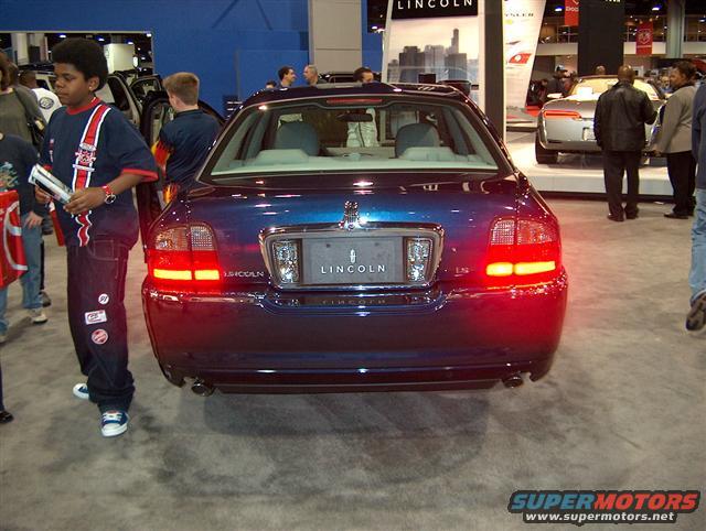Rear view of a blue Lincoln sedan at an auto show, with people around