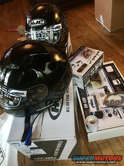 Two black HJC motorcycle helmets and boxes of accessories on a wooden floor