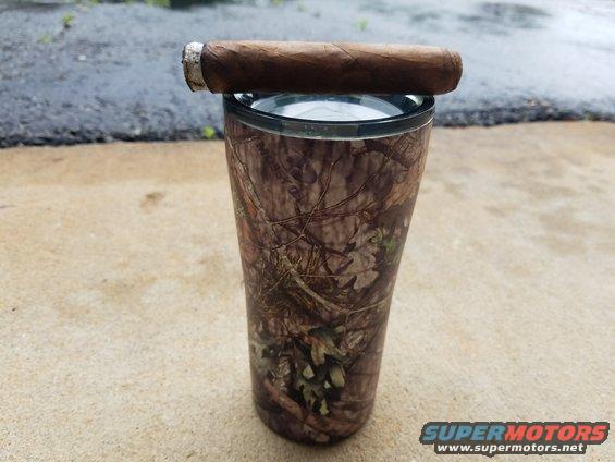 Cigar resting on top of a camouflage tumbler