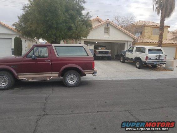 Maroon Bronco in foreground, white Bronco with spare tire in driveway, another Bronco in garage
