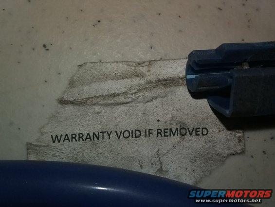 Close-up of a torn sticker that says "WARRANTY VOID IF REMOVED". A blue plastic piece is visible