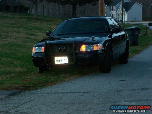 Front view of a black 2001 Ford Crown Victoria with a push bar and license plate reading 'ADAM-12'