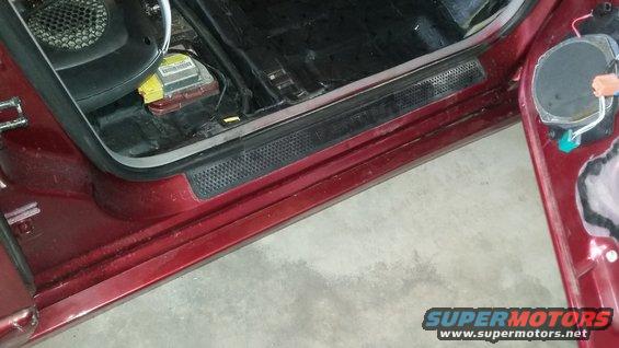 Door sill and rocker panel of dark red vehicle with battery visible