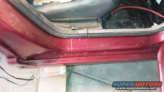 Interior shot of a red car's door sill and part of the seat. Some wires are visible