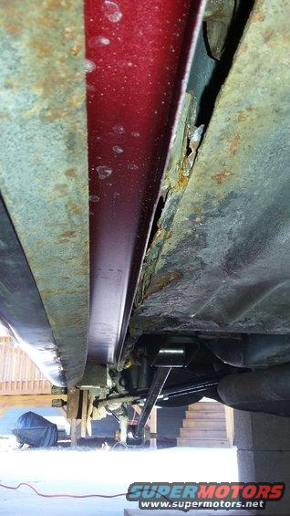 Underside view of a car showing significant rust on the rocker panel and frame components