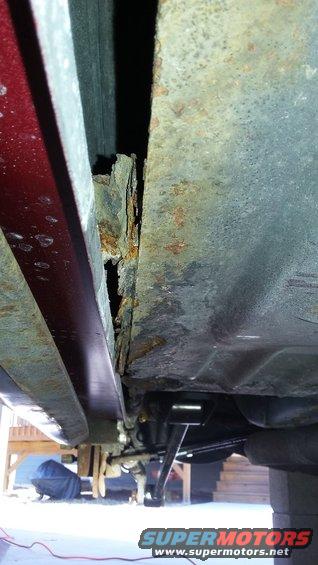 close-up of rusted metal on a vehicle's undercarriage, showing significant corrosion along the seam between body panels