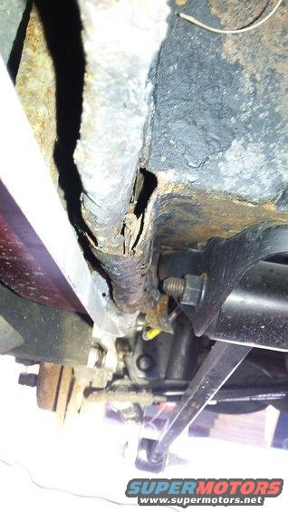 Close-up of a heavily rusted and corroded vehicle frame rail with visible damage and undercarriage components