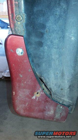 Close-up of a red plastic fender flare attached to a dark blue metal panel with visible rust and a hole
