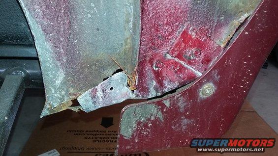 Red car's rusted lower body panel with visible corrosion and damage