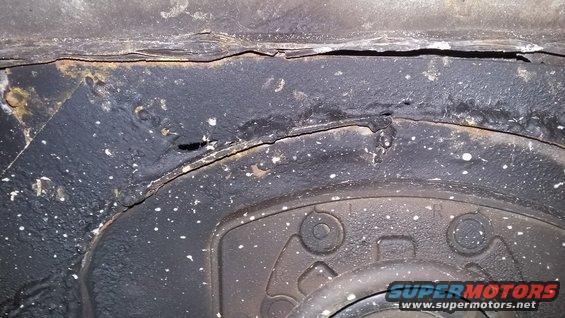 Close-up of rusted metal and part of a wheel assembly on a vehicle's undercarriage