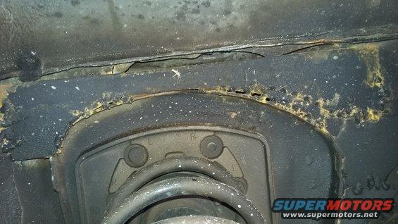 Close-up of heavily rusted metal frame and suspension component on a vehicle. Shows significant corrosion and wear
