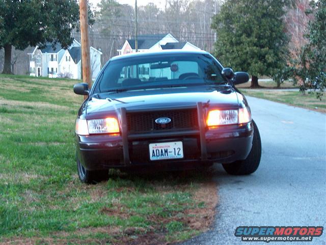 2001 Ford Crown Victoria police car with push bumper, parked on grass by a road