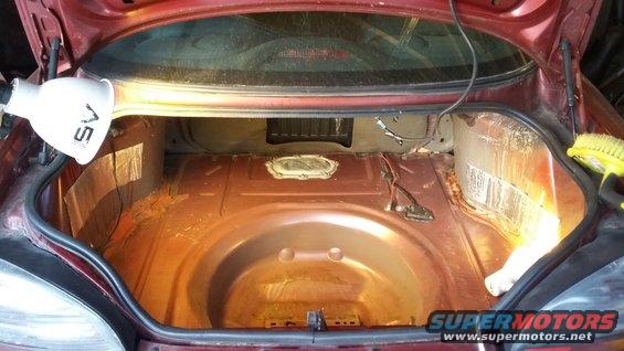 Car trunk with spare tire well, some rust, and a work light illuminating the area