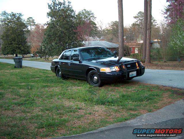 Black 2001 Ford Crown Victoria police car parked on grass, front quarter view, with a push bumper and light bar