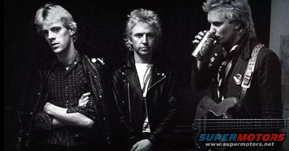 Three men in leather jackets, one drinking from a can and holding a guitar