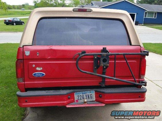 Rear view of a red 1996 Ford Bronco with a tan top and a spare tire carrier mounted on the back