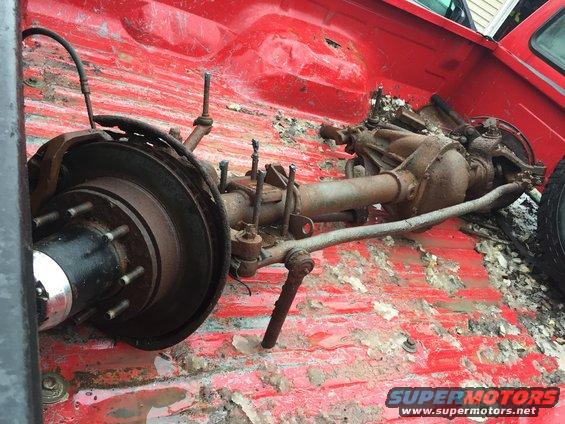 Rear axle assembly with brake components and suspension links, lying in the bed of a red pickup truck