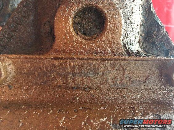 Brown cast iron part with stamped numbers and letters, some obscured by rust