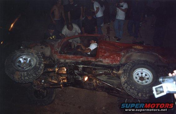 Red off-road vehicle overturned on its side with people gathered around