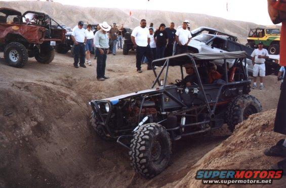 Custom off-road buggy with exposed engine and roll cage, driving through a dirt track