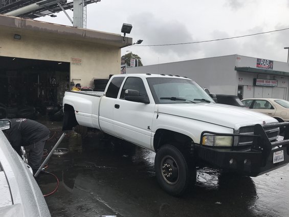 1997 Dodge 3500 dually pickup truck parked outside a garage with a man working on the front wheel