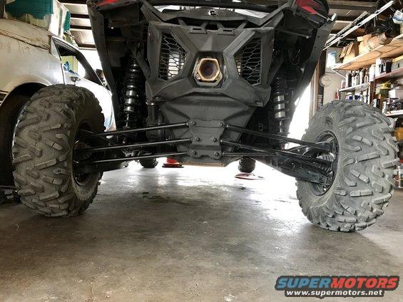 Rear suspension and tires of a side-by-side ATV parked next to another vehicle