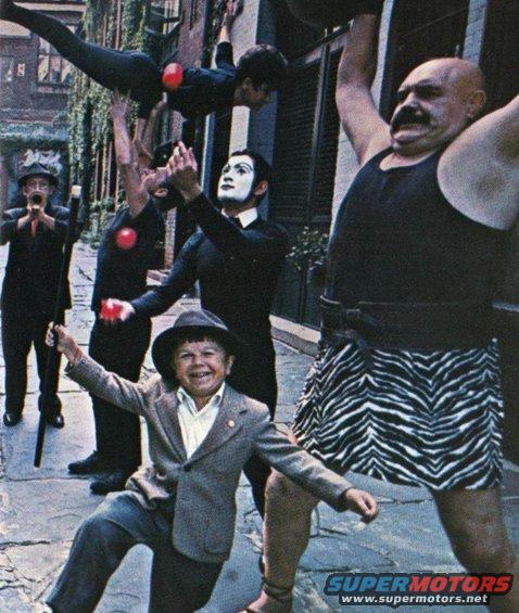 Circus performers and a child in a street scene. A strongman lifts a weight while others juggle