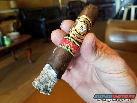 Hand holding a lit cigar with '20th Anniversary' band