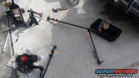 Steering linkage and power steering gear on concrete with tools and a jack