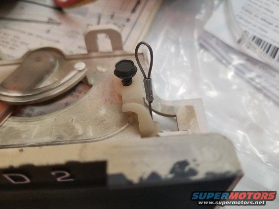 Close-up of a white plastic bracket with a black screw and wire loop attached to a beige and black component with "D 2" visible