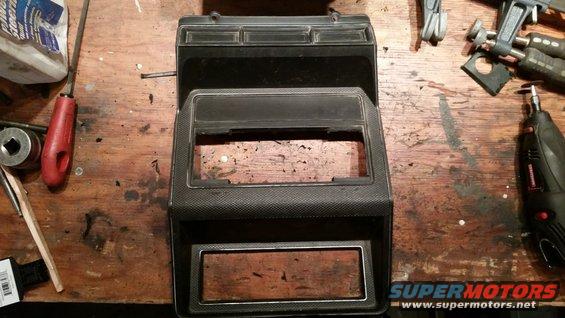 Car dashboard center console part on a wooden workbench with tools including a Dremel and screwdrivers