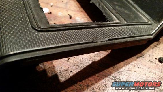 Black textured dashboard trim piece with a rectangular cutout, resting on a wooden surface