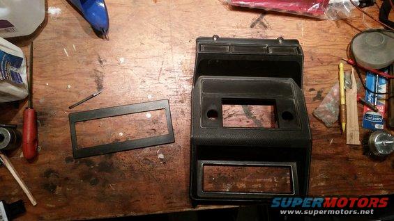 Car dashboard trim pieces and a radio bezel on a wooden surface with tools