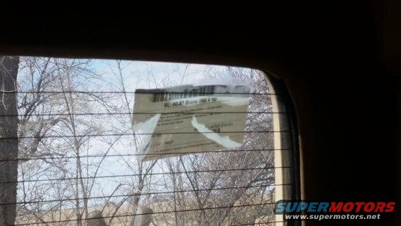 Sticker on a rear window reads 'BL-80-47 Bronco 1984 1985'. Trees and sky visible through the window